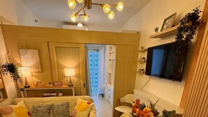 A modern living room with a sofa, a dining table set with plates, a TV mounted on the wall, and a view of the outside. - Fourth's Jazz Cozy Pad (Makati)