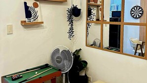 A living room with a pool table, a fan, a couch, and decorative items on shelves. - Fourth's Jazz Cozy Pad (Makati)