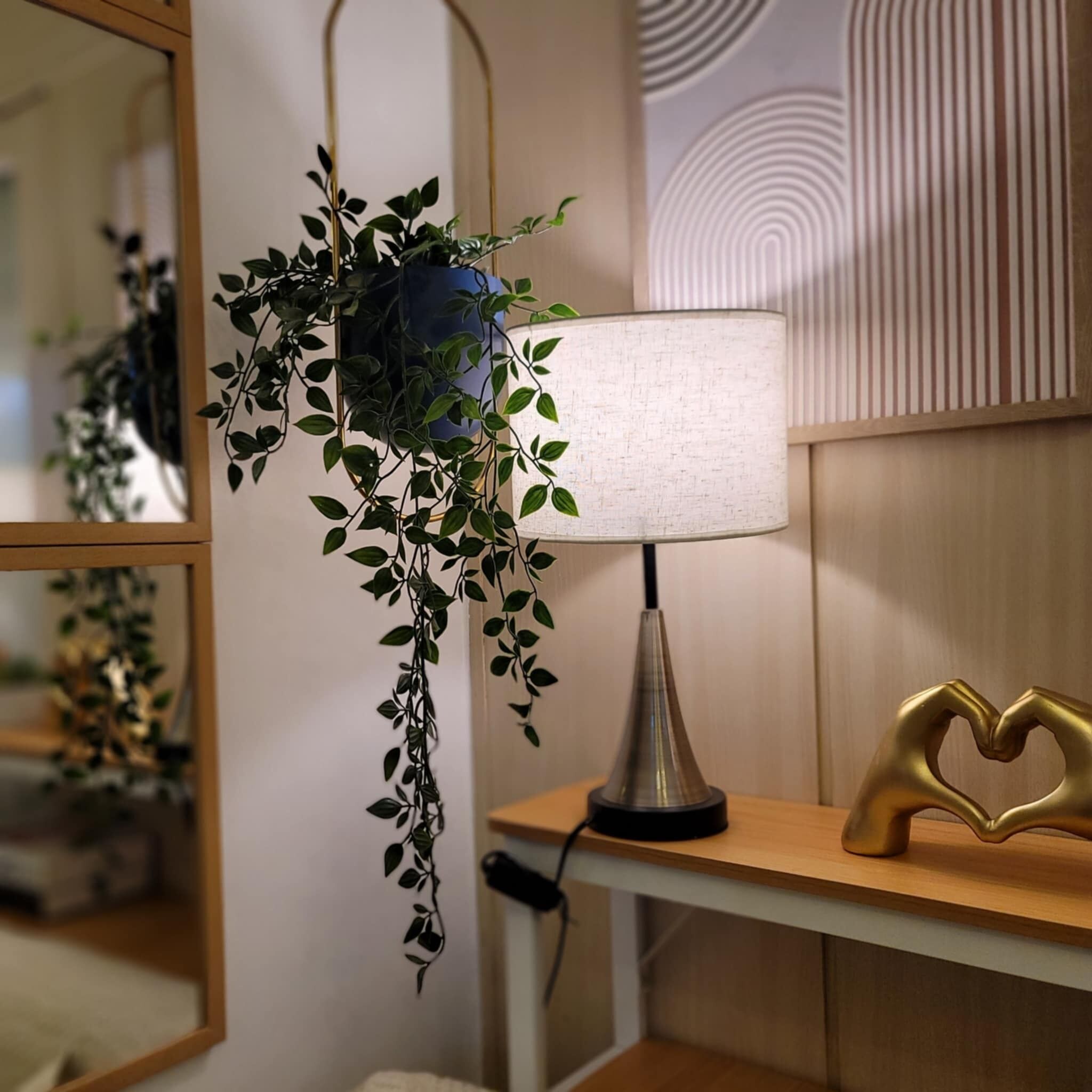 Ein Nachttisch mit Lampe, einer herzförmigen Dekoration und einer hängenden Pflanze.