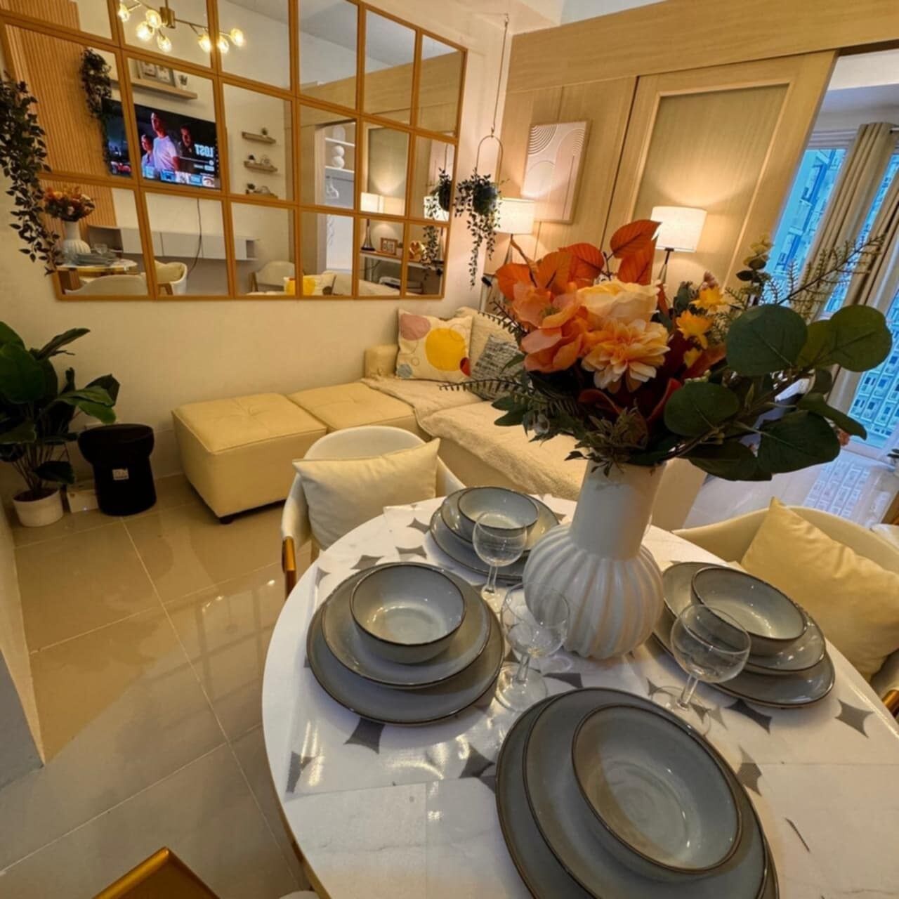 A dining area with a round table set for four, surrounded by a sofa and a TV in the background.