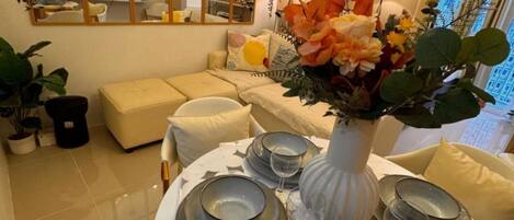 A dining area with a round table set for four, surrounded by a sofa and a TV in the background.