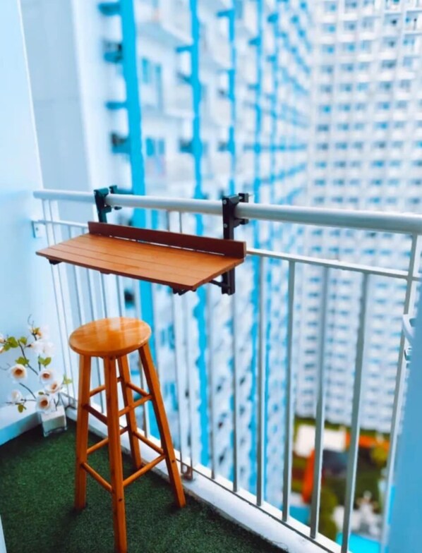 Un balcón con un taburete de madera y una mesita.
