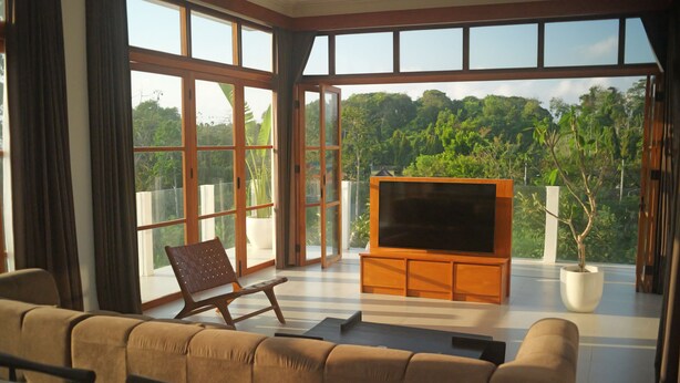 Un ampio soggiorno con una grande TV, posti a sedere confortevoli e un balcone con vista su una rigogliosa vegetazione.
