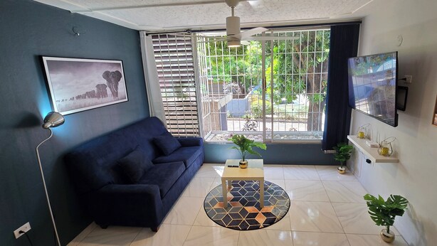 A living room with a dark blue sofa, a round coffee table, and a large window with metal bars. - The Central Comfort in Kingston (Kingston)