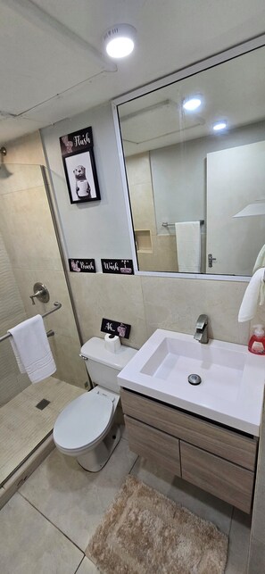 A modern bathroom with a white sink, toilet, and shower. There is a large mirror above the sink and a framed picture on the wall. - The Central Comfort in Kingston (Kingston)