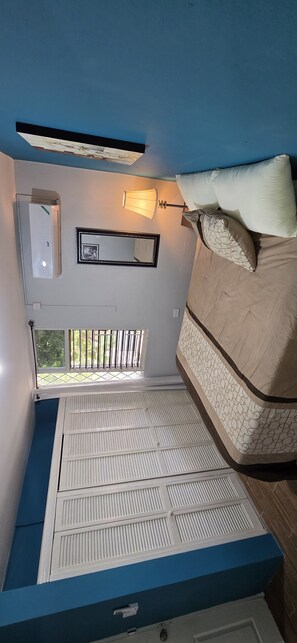 A bedroom with a bunk bed, a bedside lamp, a wall-mounted air conditioner, and a window with bars. - The Central Comfort in Kingston (Kingston)