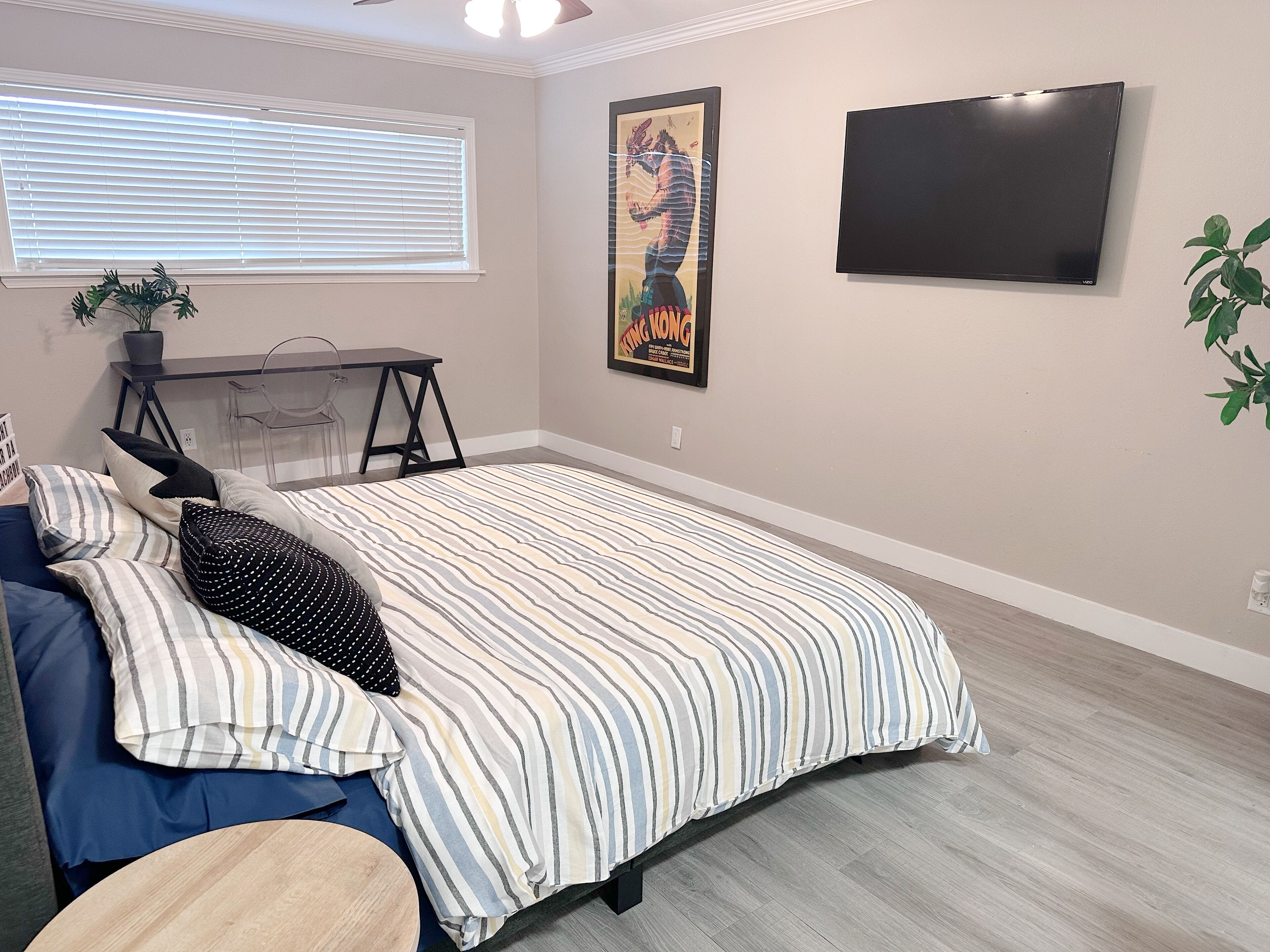 Quarto com cama, escrivaninha, cadeira, televisão e janela com persianas.