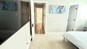 Quarto com uma cama, uma porta e um corredor que dá para outro cômodo.