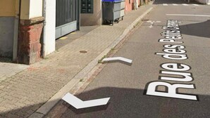 Eine Straße mit Gebäuden, eines davon mit einem Balkon und einer Mülltonne.