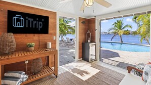 Une chambre d’hôtel avec une console en bois, un téléviseur affichant le logo iTrip, un ventilateur de plafond et une vue sur une piscine et des palmiers.