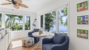 Un salon moderne avec vue sur l’océan, doté d’un ventilateur de plafond et orné d’œuvres d’art.