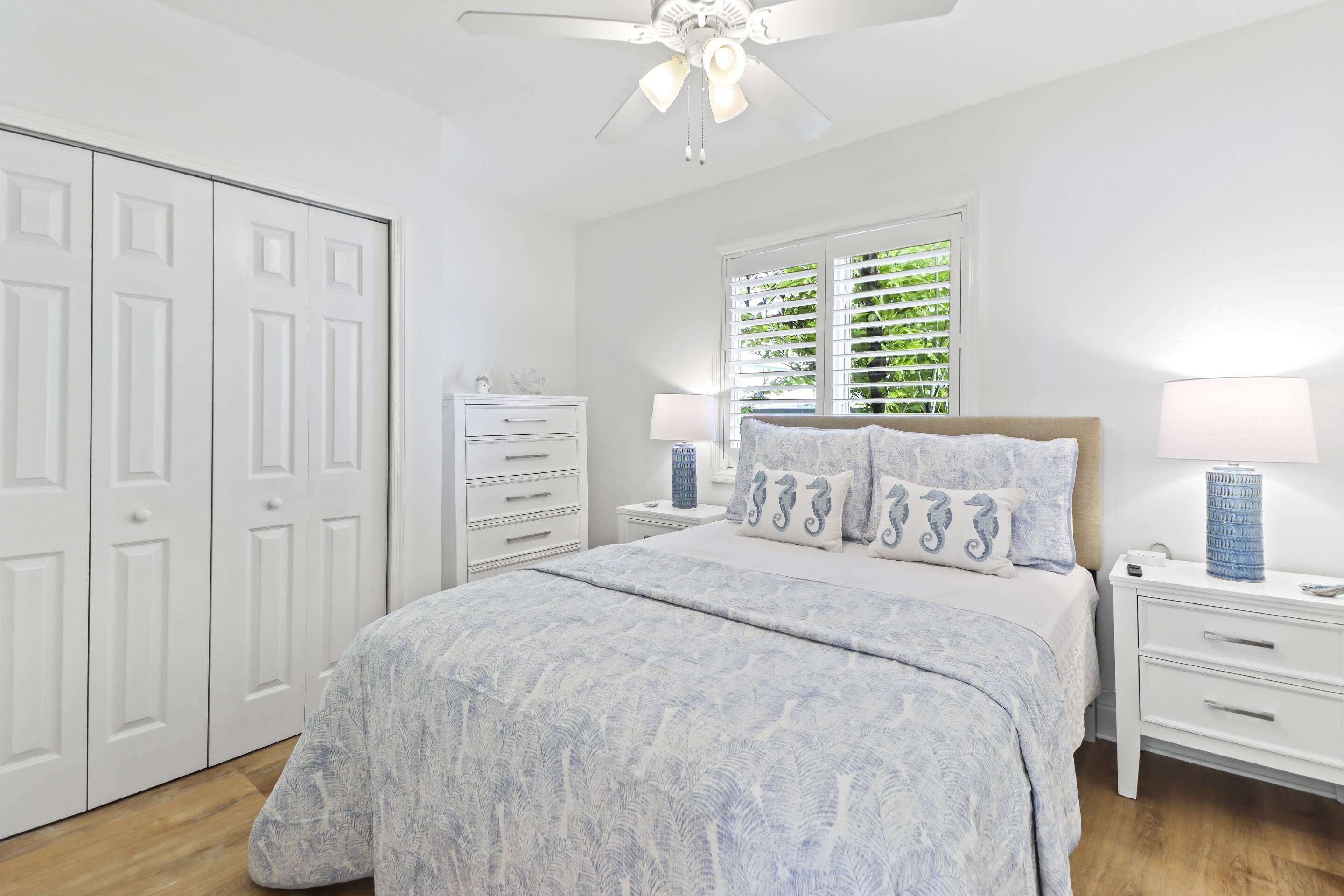 A bedroom with a bed, nightstands, a dresser, a ceiling fan, and a window with blinds.