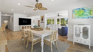 Un salon moderne avec un coin repas, des meubles blancs et un ventilateur de plafond.