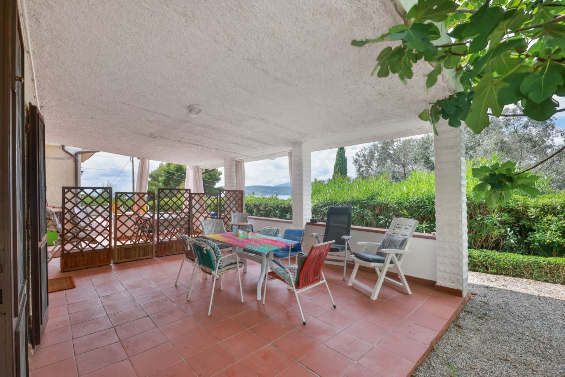 An outdoor patio with a table and chairs, a view of greenery and hills, and a white ceiling.