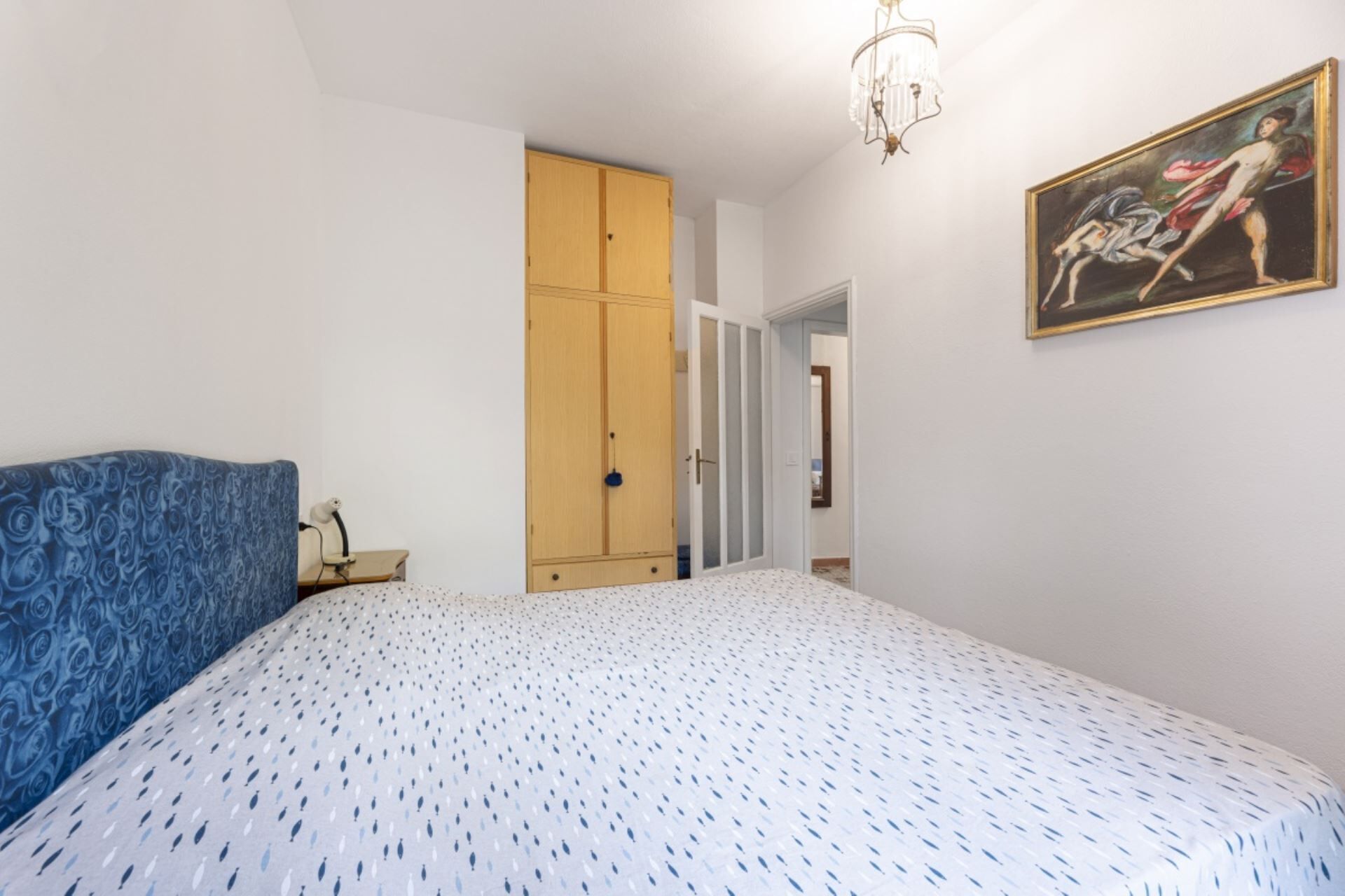 Une chambre à coucher avec un lit, une armoire, un tableau et un lustre.