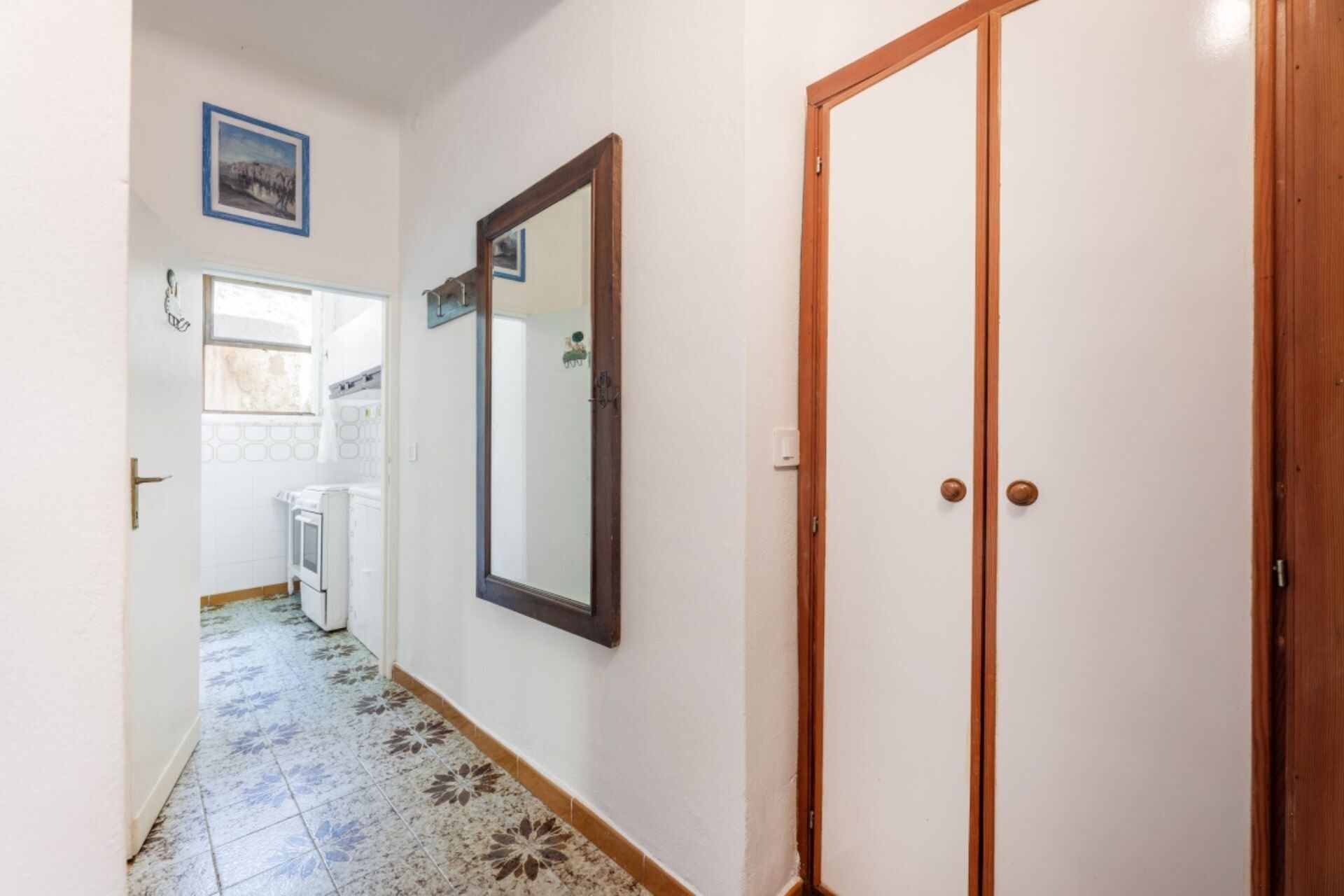 Un couloir avec un sol carrelé, une porte en bois et un miroir accroché au mur.