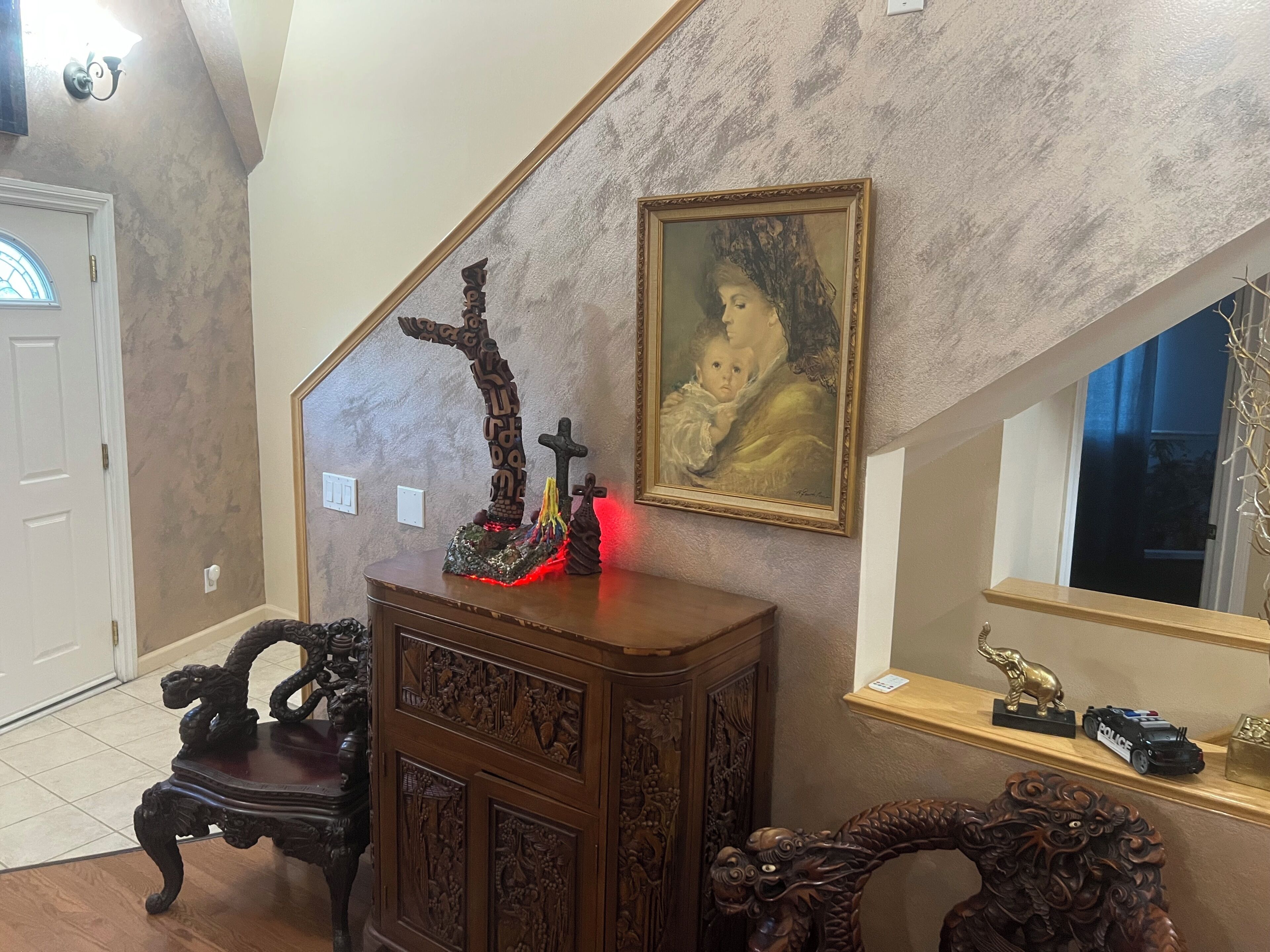 A staircase with a wooden carved cabinet and a painting on the wall.