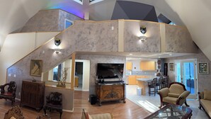 Ein geräumiges Loft mit hoher Decke, einer Galerieebene, einem großen Fernseher und einer Küchenzeile.