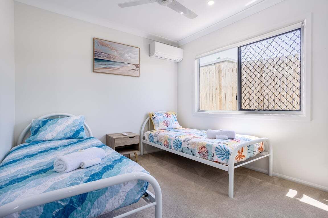 A bedroom with two beds, a window with a view, an air conditioning unit, and a ceiling fan.