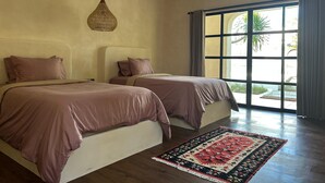 Une chambre avec deux lits, un luminaire en fibres tressées, une grande fenêtre avec des rideaux et un tapis à motifs.