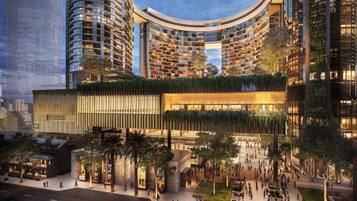 A modern hotel with a curved facade, multiple balconies, and a spacious outdoor area with trees and seating.