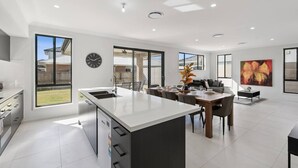 A modern kitchen with a central island, dining area with chairs, and a living space with a sofa. - Spacious 6BR Home Near Beach in Victoria Point (Victoria Point)