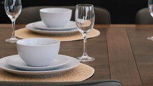 A dining table set with white plates, bowls, and wine glasses, with a modern kitchen in the background. - Spacious 6BR Home Near Beach in Victoria Point (Victoria Point)