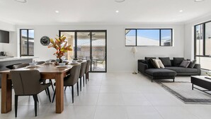 A modern living room with a dining area, a sofa, and a large window. - Spacious 6BR Home Near Beach in Victoria Point (Victoria Point)