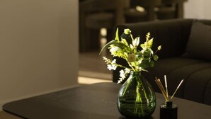 A living room with a dark-colored sofa, a glass vase with flowers on a table, and a lamp in the background. - Spacious 5BR Home in Heart of Sunnybank |Sleeps 10 (Sunnybank)