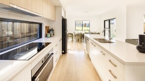 A modern kitchen with a central island, stainless steel appliances, and a view to the dining area. - Spacious 5BR Home in Heart of Sunnybank |Sleeps 10 (Sunnybank)
