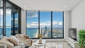 A modern living room with a large window offering a city and beach view, a sofa, a coffee table, and a TV on a stand.