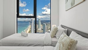 A bedroom with a large window offering a city view, a bed with white linens, and a gray headboard.