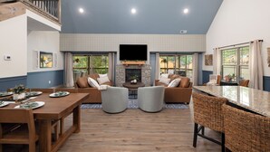 A spacious living area with a fireplace, comfortable seating, a dining table set for four, and large windows offering a view of the outdoors. - Ledgerock Cabin – Elegant 3BR Retreat in Tall Timbers Resort (Hollister)