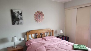 A bedroom with a wooden headboard, a pink bedspread, a green throw, a nightstand with a lamp, and a wall decoration. - Apartment 3 Bedrooms | next to Delgado Clinic in Miraflores (Miraflores)