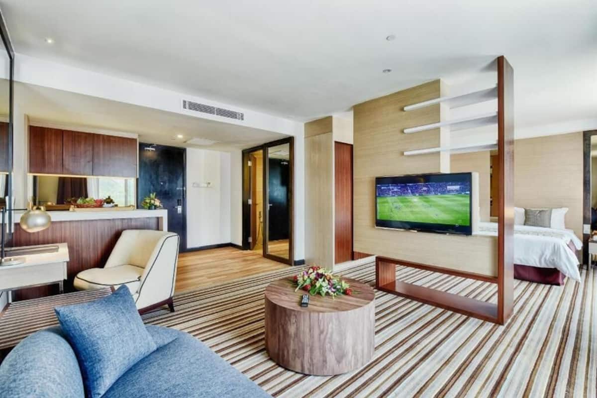 Una habitación de hotel moderna con una televisión grande, un sofá, una mesa de centro y una cama.