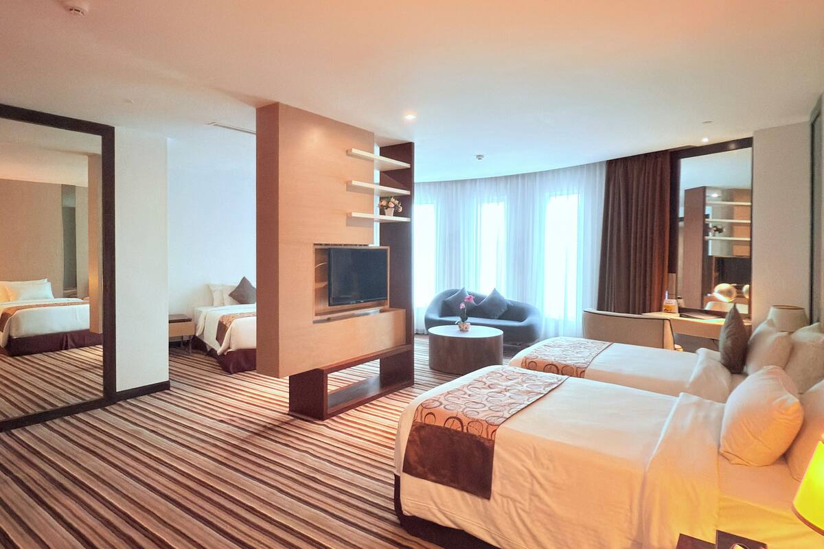 Habitación de hotel con dos camas, televisión, sofá, mesa de centro y un espejo grande.