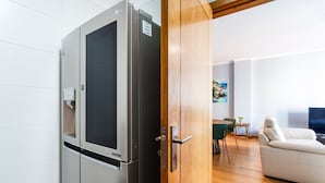 Eine moderne Küche mit einem eingebauten LG-Kühlschrank, einer Holztür und einem Essbereich mit einem weißen Sofa und einem kleinen Tisch.