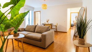 Un soggiorno moderno con un divano beige, pavimento in legno e piante verdi di grandi dimensioni.