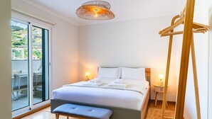 Camera d'albergo con un letto, comodini, una panca, una lampada a sospensione e vista su un balcone.