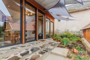A modern house with a stone-paved entrance, large glass doors, and a garden with various plants and flowers. - Nora Guest House 2BR & Garden (Nagygörbő)