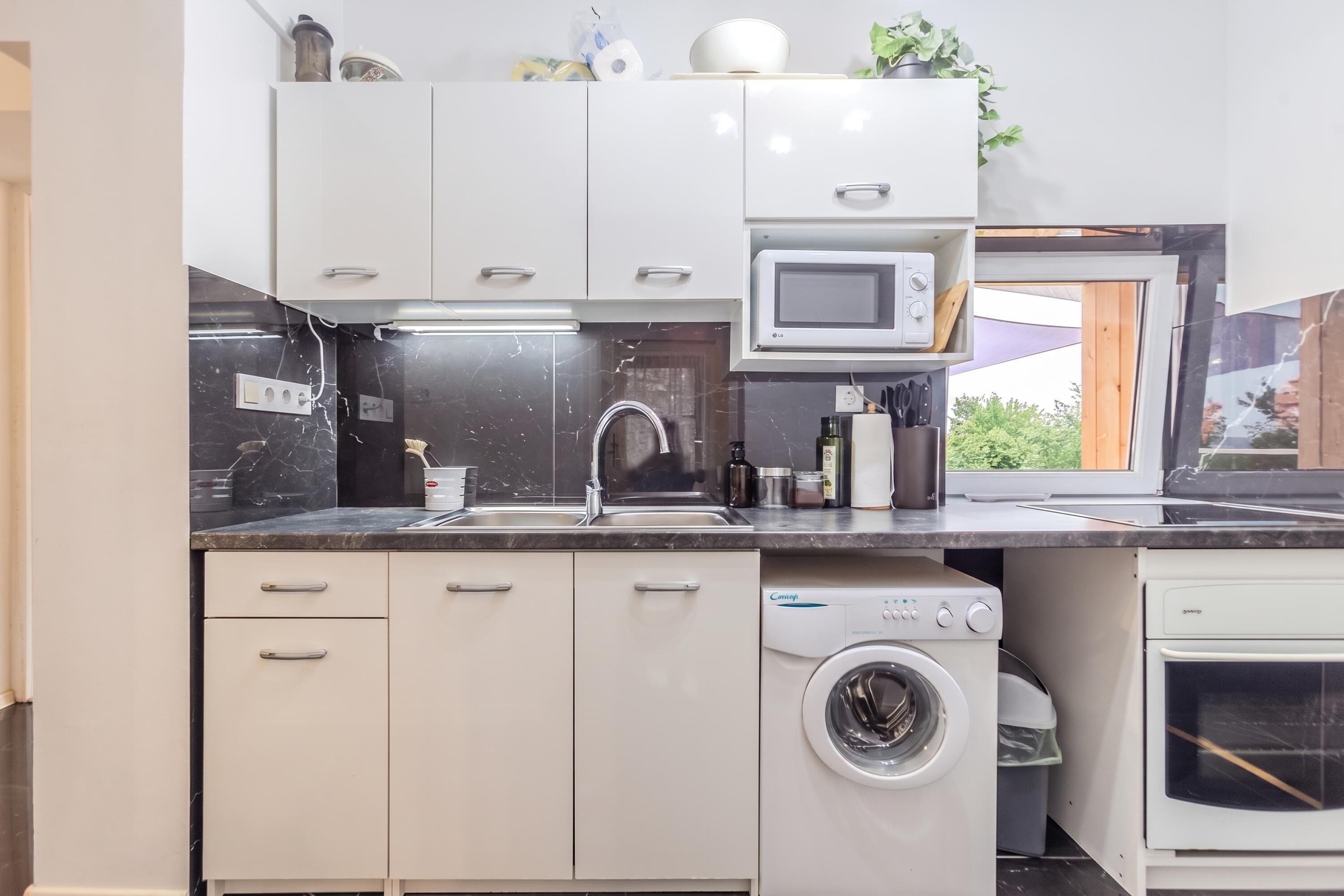 Ett modernt kök med vita skåp, en inbyggd mikrovågsugn, en diskho och en tvättmaskin.