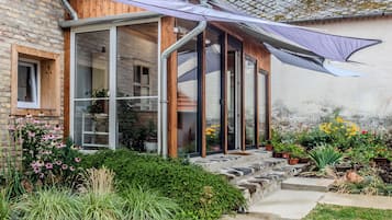 A house with a glass conservatory, wooden exterior, and a garden with various plants and flowers.