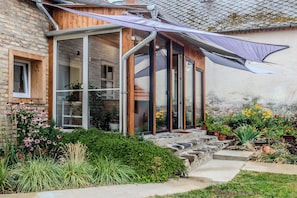 A house with a glass conservatory, wooden exterior, and a garden with various plants and flowers. - Nora Guest House 2BR & Garden (Nagygörbő)