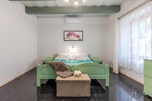 A room with a bed, a bedside table, a green bench, a framed picture on the wall, and a window with curtains. - Nora Guest House 2BR & Garden (Nagygörbő)
