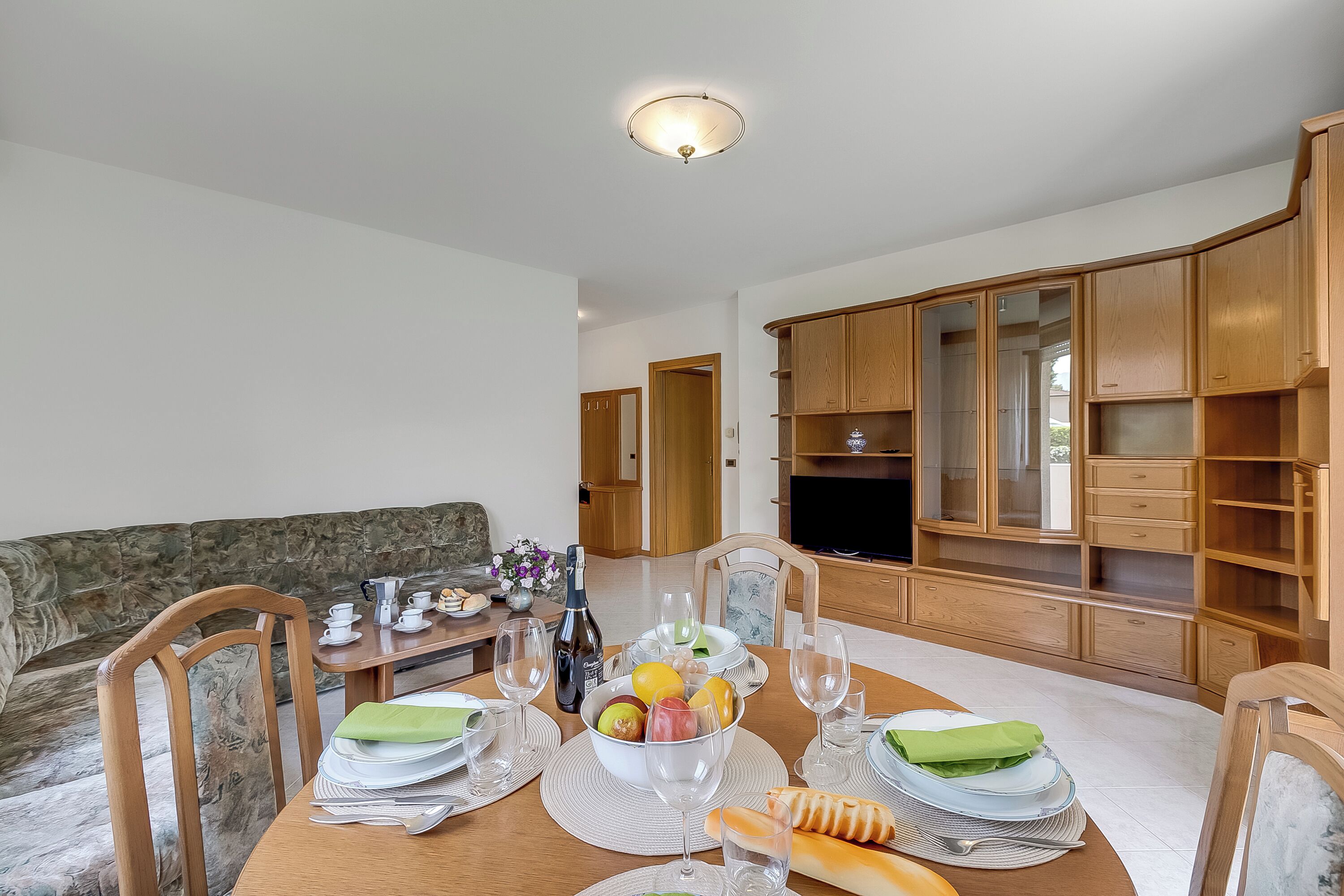 Uma sala de jantar com uma mesa de madeira posta para refei ção, rodeada por armários de madeira e uma televisão.