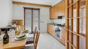 A modern kitchen with wooden cabinets, a dining area with a table set for four, and a sliding glass door leading to a balcony. - The Olive Tree Garden With Mountain View (Arco)