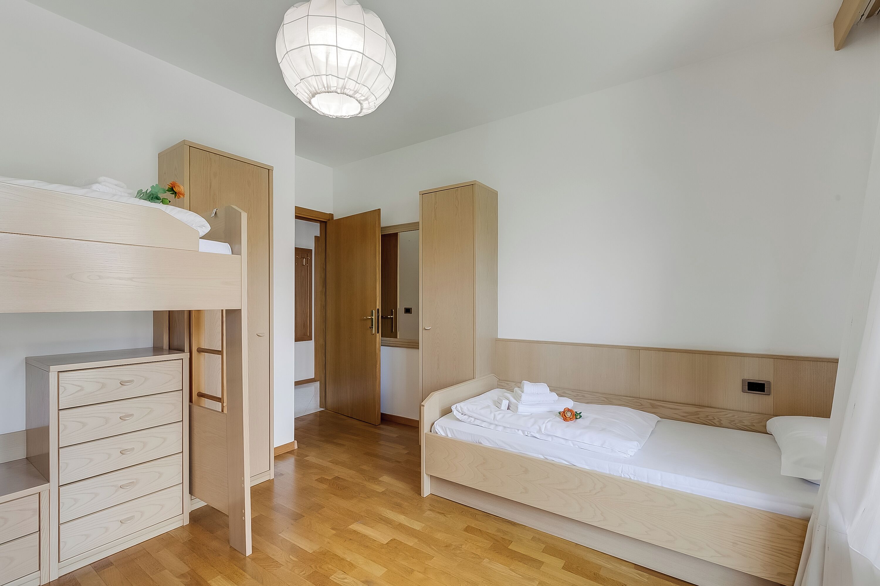 A room with a bunk bed, a single bed, wooden furniture, and a hanging light fixture.