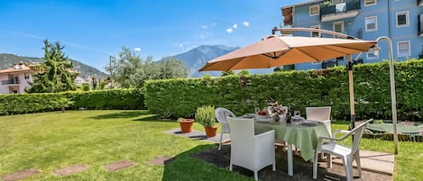A well-maintained outdoor dining area with a table set for two, surrounded by lush greenery and a view of a mountain range.