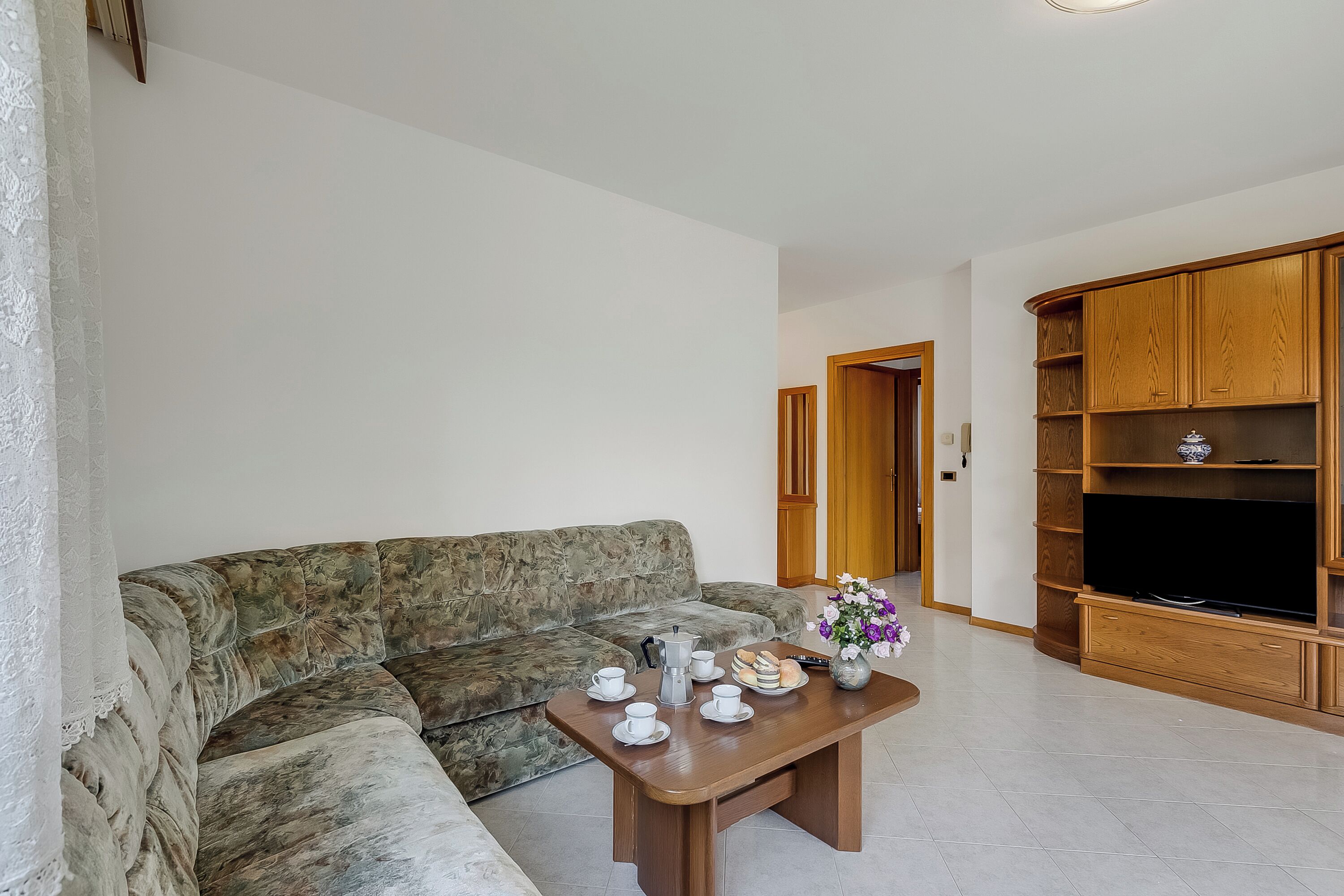 A living room with a sofa, a coffee table with cups and a vase, and a wooden entertainment unit.