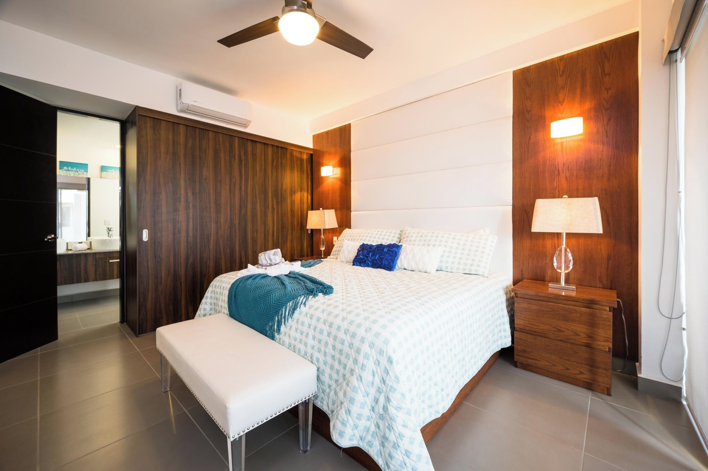 A modern bedroom with a bed, bedside tables, a bench, and a ceiling fan.
